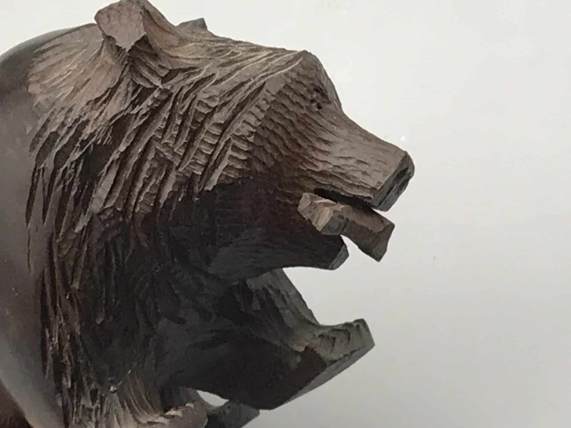 Close-up side profile of a hand-carved hardwood bear in Kibori Kuma style, showing detailed fur and fish in its mouth.