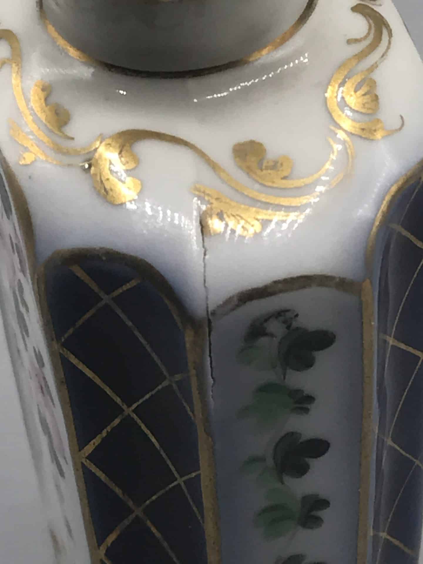 19th century French porcelain scent bottle showing hand painted floral panel, gilt scroll decoration, and visible firing flaw crack on the shoulder